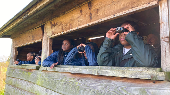 School children in Farms for City Children overalls in a bird hide with binoculars
