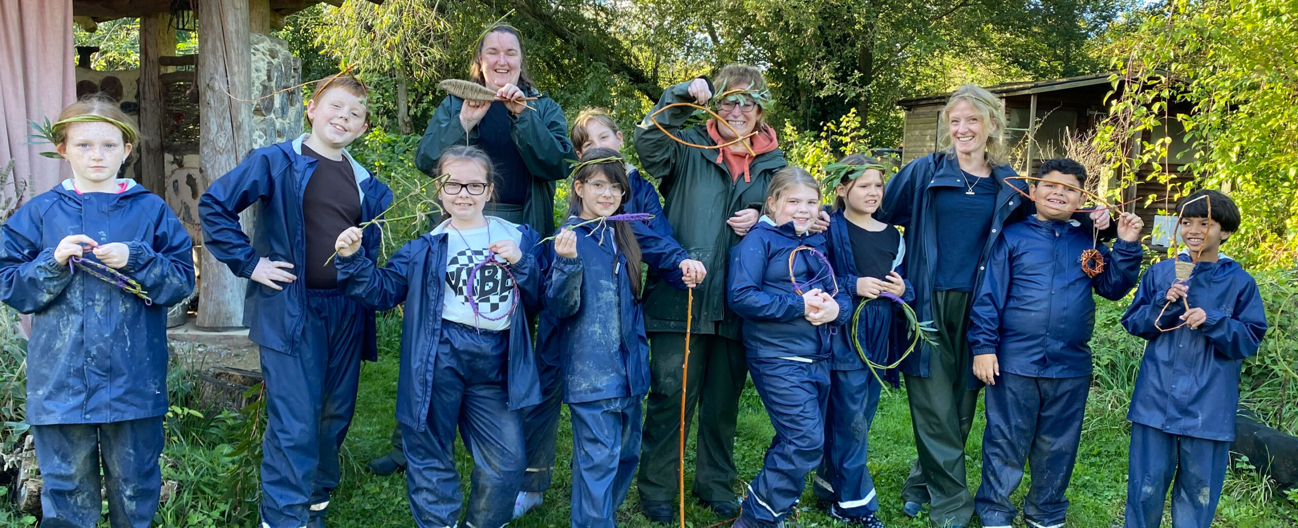 Group of school children in farm overalls holding woodland craft items.
